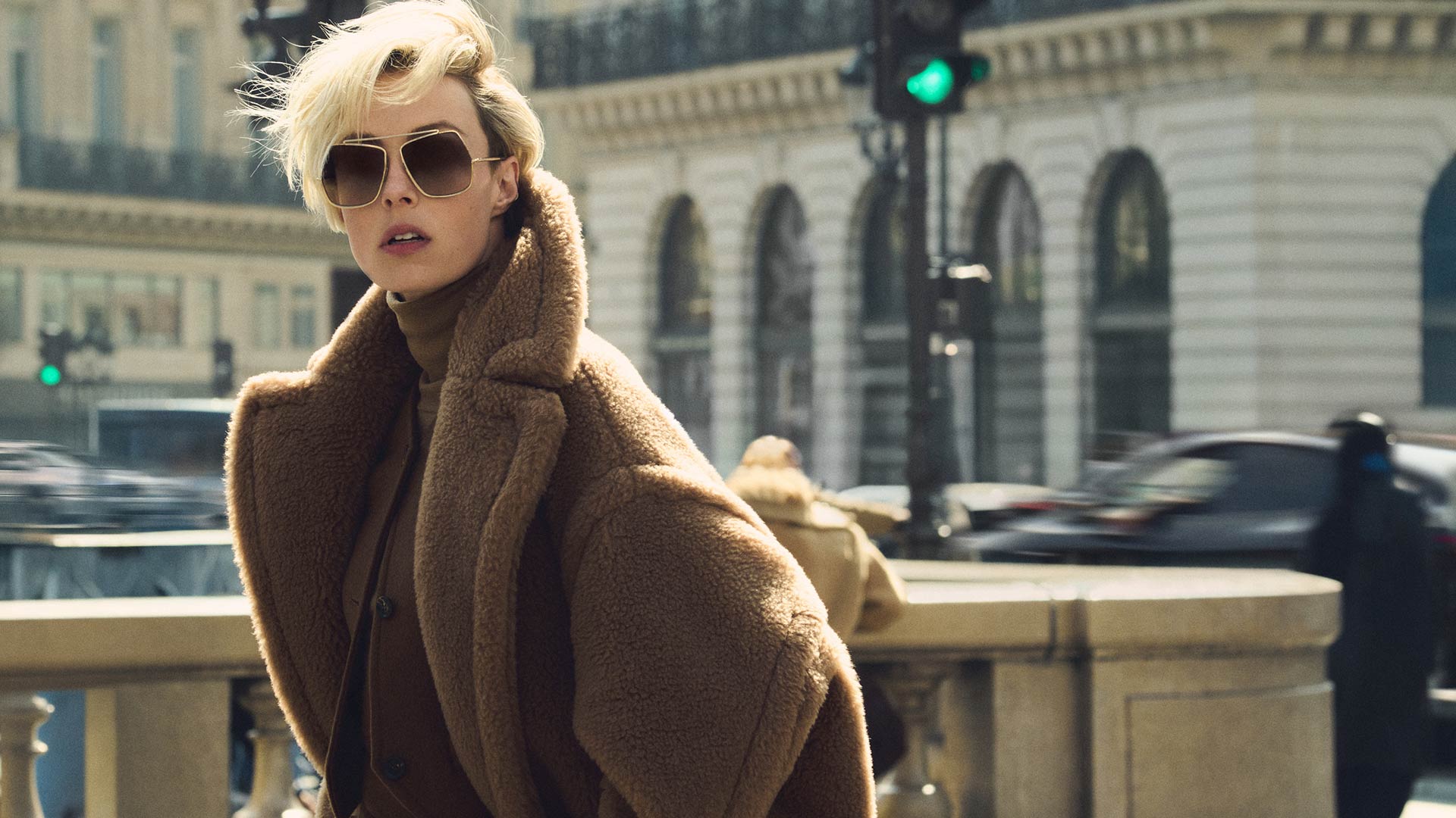 Das Model trägt den legendären langen Teddy Bear Mantel von Max Mara im Farbton Kamel in einer dynamischen, städtischen Umgebung.